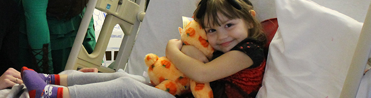 Child on hospital bed hugging a stuffed animal.