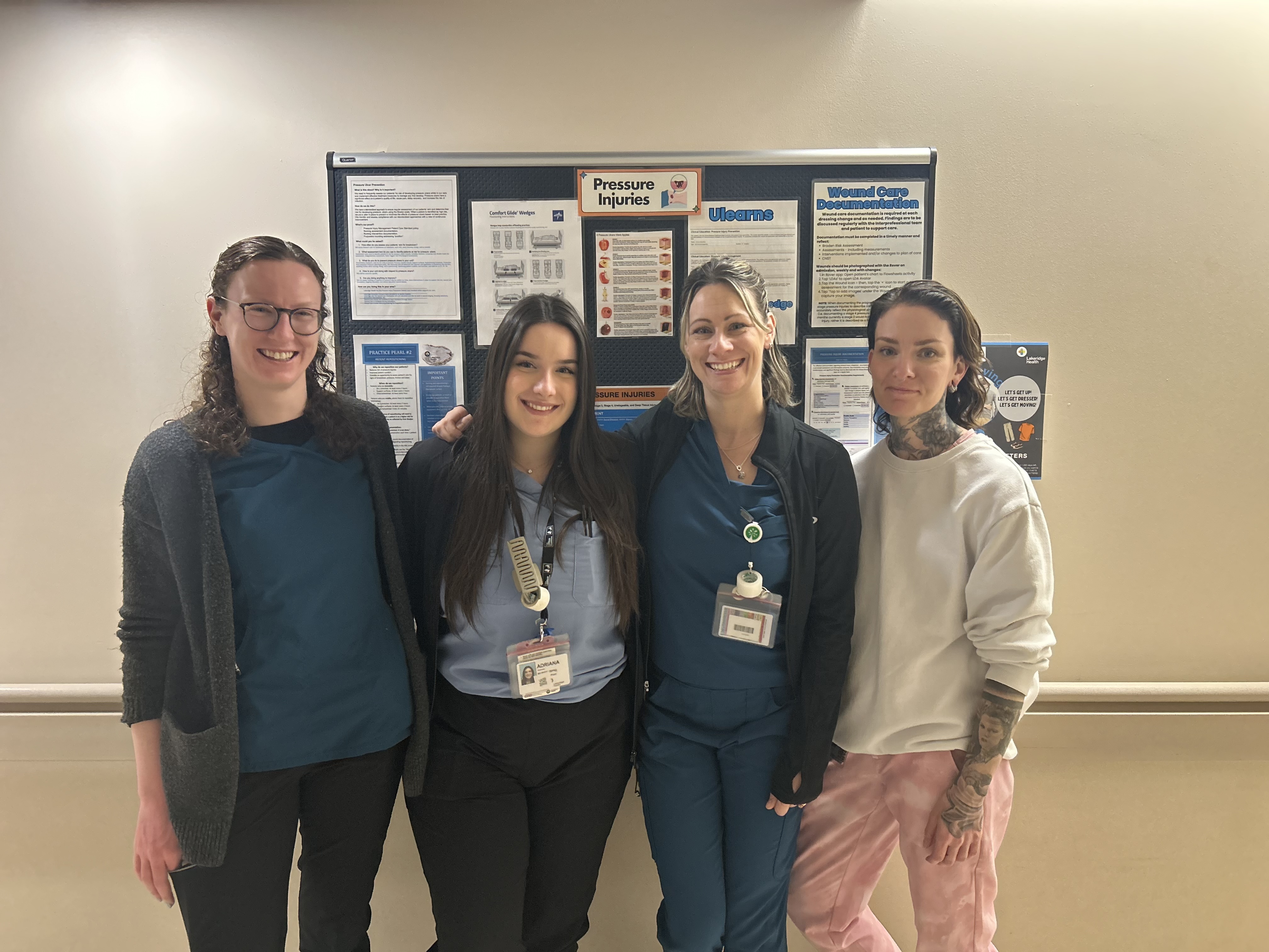 Four nurses standing in front of education bulletin board on a unit.