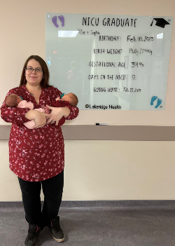 Proud Mother Amanda Mackenzie poses with her twins in front of Oshawa Hospital's new NICU Graduate Board